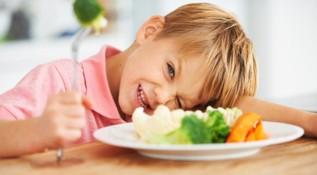 Portrait of a cute young boy looking naughty while holding a piece of broccoli on his fork