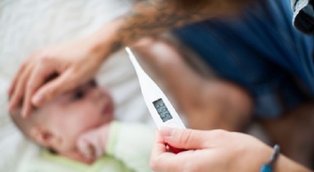 E08B4M Cropped image of mother examining baby boy's temperature in bed